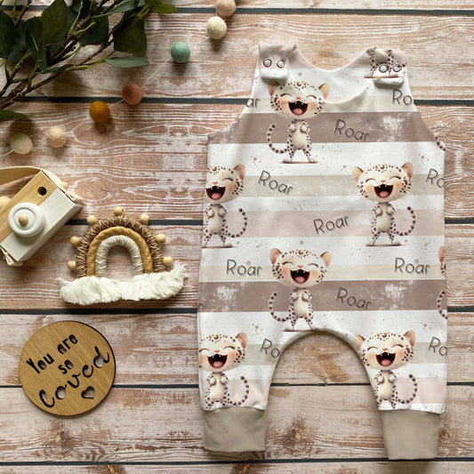 Handgenähter Baby-Strampler im Leo-Design in Beige mit „Roar“-Druck, weich und bequem aus French Terry, perfekt für Babys – liebevoll dekoriert mit Holzkamera, Makramee-Regenbogen und Naturdekoration.